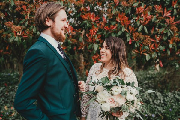 bride and groom have a first look and are laughing in front of a red bush, styal lodge wedding photography, styal lodge wedding photographer, manchester wedding photographer, manchester wedding photography, cheshire wedding photographer, cheshire wedding photography