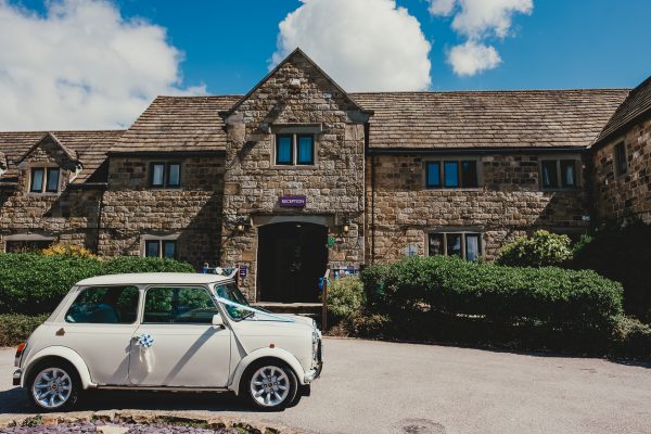 a vintage white mini parked outside a hotel on a wedding day