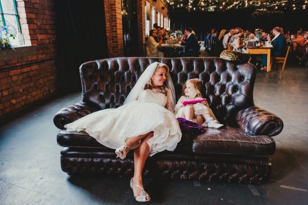 bride sits on sofa with a little girl as they look and smile at each other, elsecar heritage centre wedding photographer, elsecar heritage centre wedding photography, elsecar heritage centre wedding, ayesha photographer, manchester wedding photographer, manchester wedding photography, sheffield wedding photographer, sheffield wedding photography, barnsley wedding photographer, innercity weddings